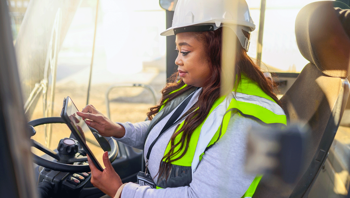 Une femme portant un casque de chantier blanc et un gilet de sécurité conduit un chariot élévateur