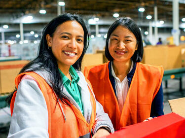 Deux femmes souriantes portant des gilets orange dans un entrepôt